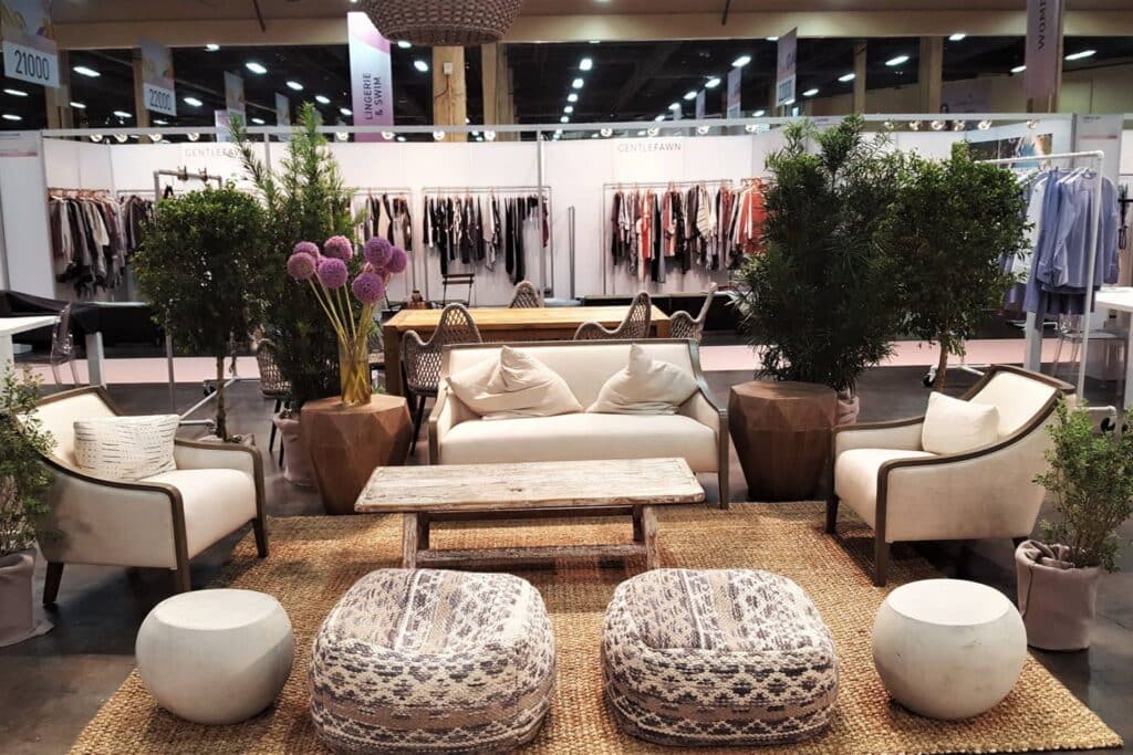 lounging space with chairs, tables, and plants inside a trade show exhibit hall