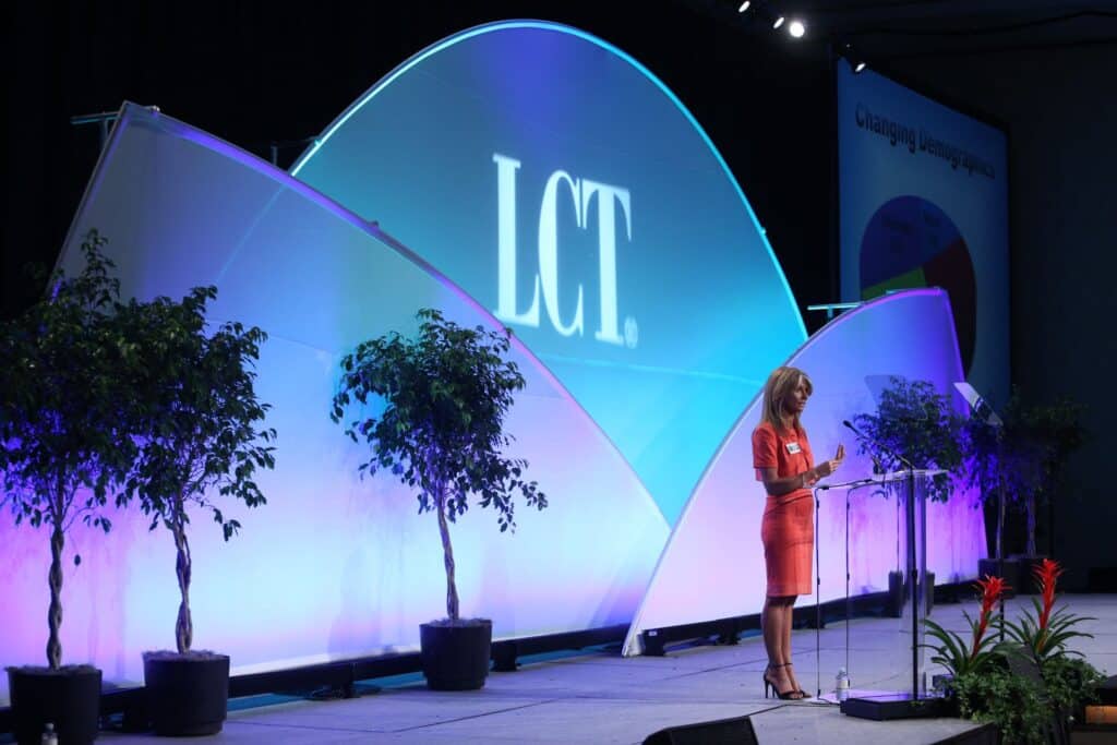 woman in an orange dress standing on a stage during a business presentation at a trade show