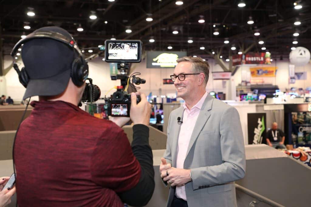 a man talking in front of a videographer at a trade show