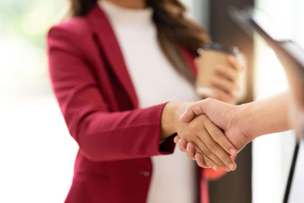 person in a red blazer shaking hands with someone in the foreground